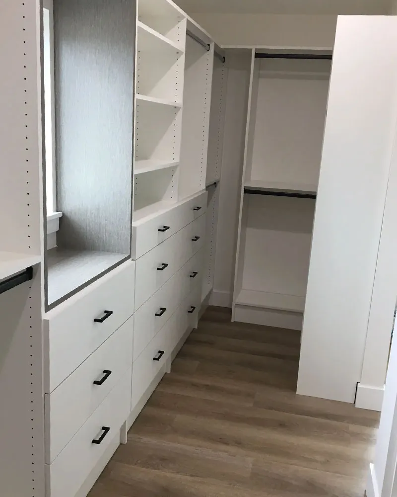 Custom white reach-in closet with a grey textured back panel, window seat, and matte-black handles in a Pinellas County home